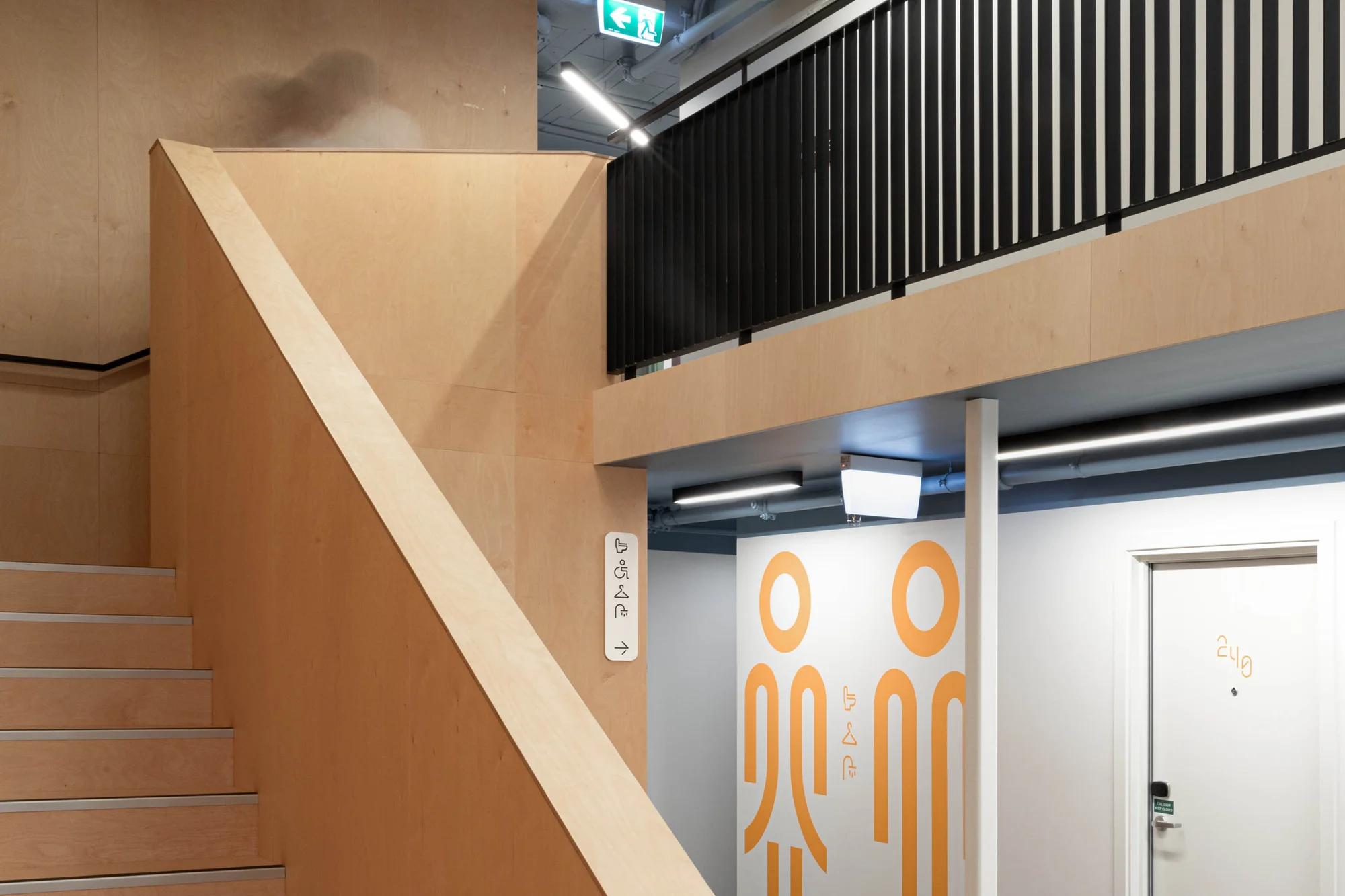 Interior view of modern hallway with wooden stairs, gender-neutral restroom signage, and contemporary design elements.