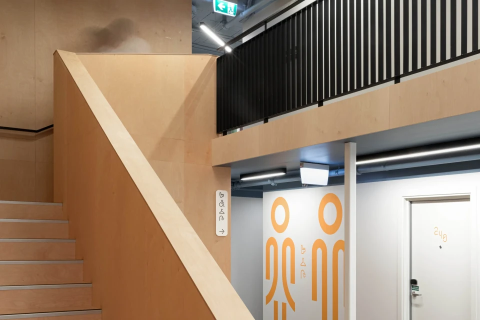 Interior view of modern hallway with wooden stairs, gender-neutral restroom signage, and contemporary design elements.