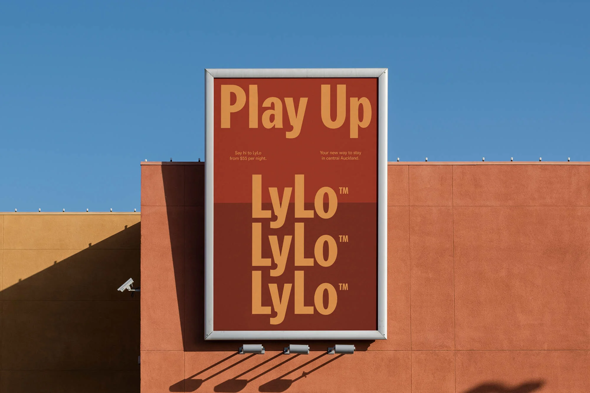 Outdoor billboard featuring the LyLo hotel advertisement with the text 'Play Up' and 'LyLo' repeated, set against a clear blue sky and a commercial building.