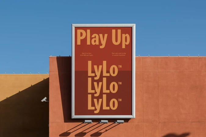 Outdoor billboard featuring the LyLo hotel advertisement with the text 'Play Up' and 'LyLo' repeated, set against a clear blue sky and a commercial building.