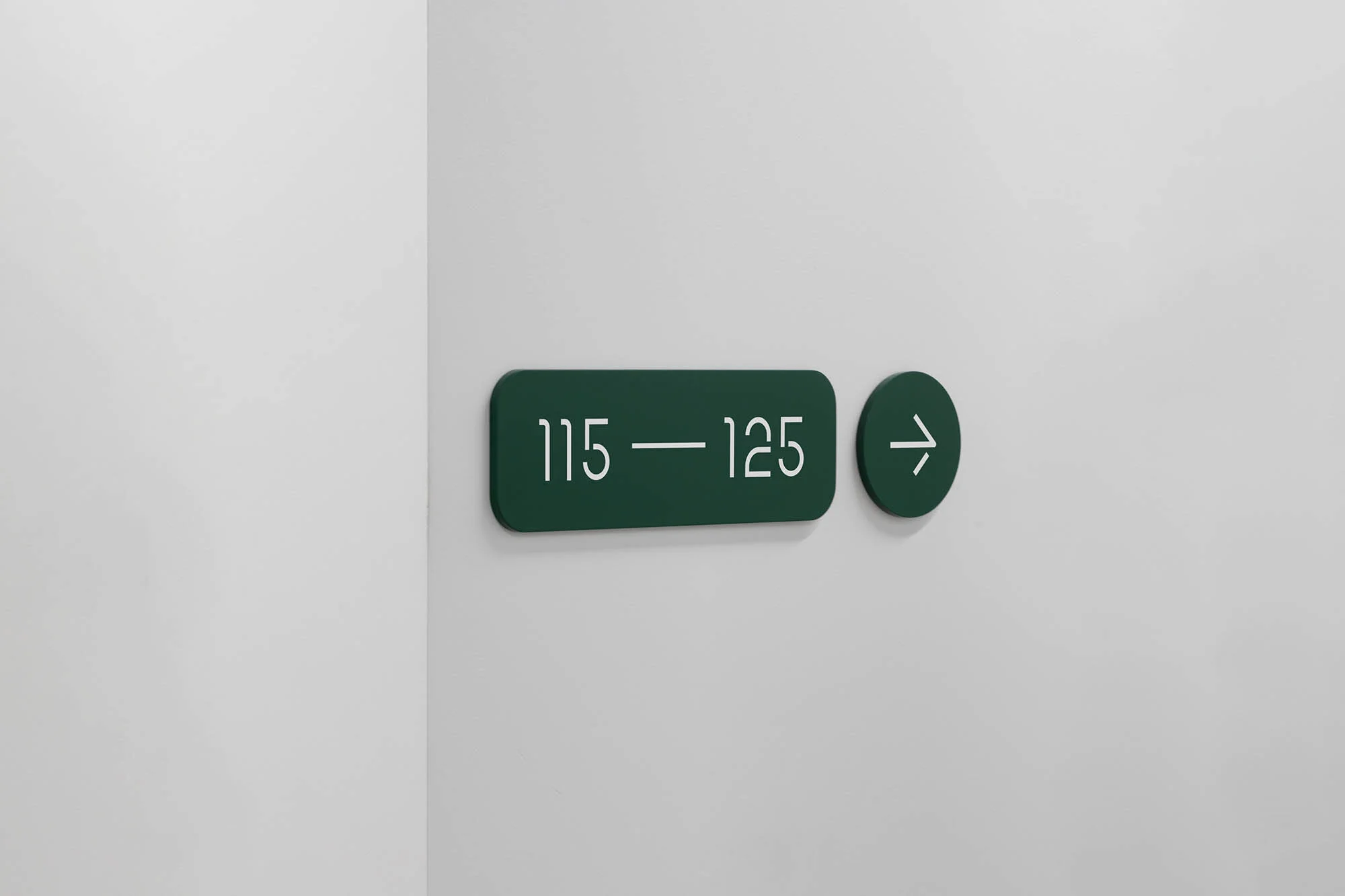 Dark green sign on a white wall indicating room numbers 115 to 125, with a right-pointing arrow indicating direction; simple modern design.