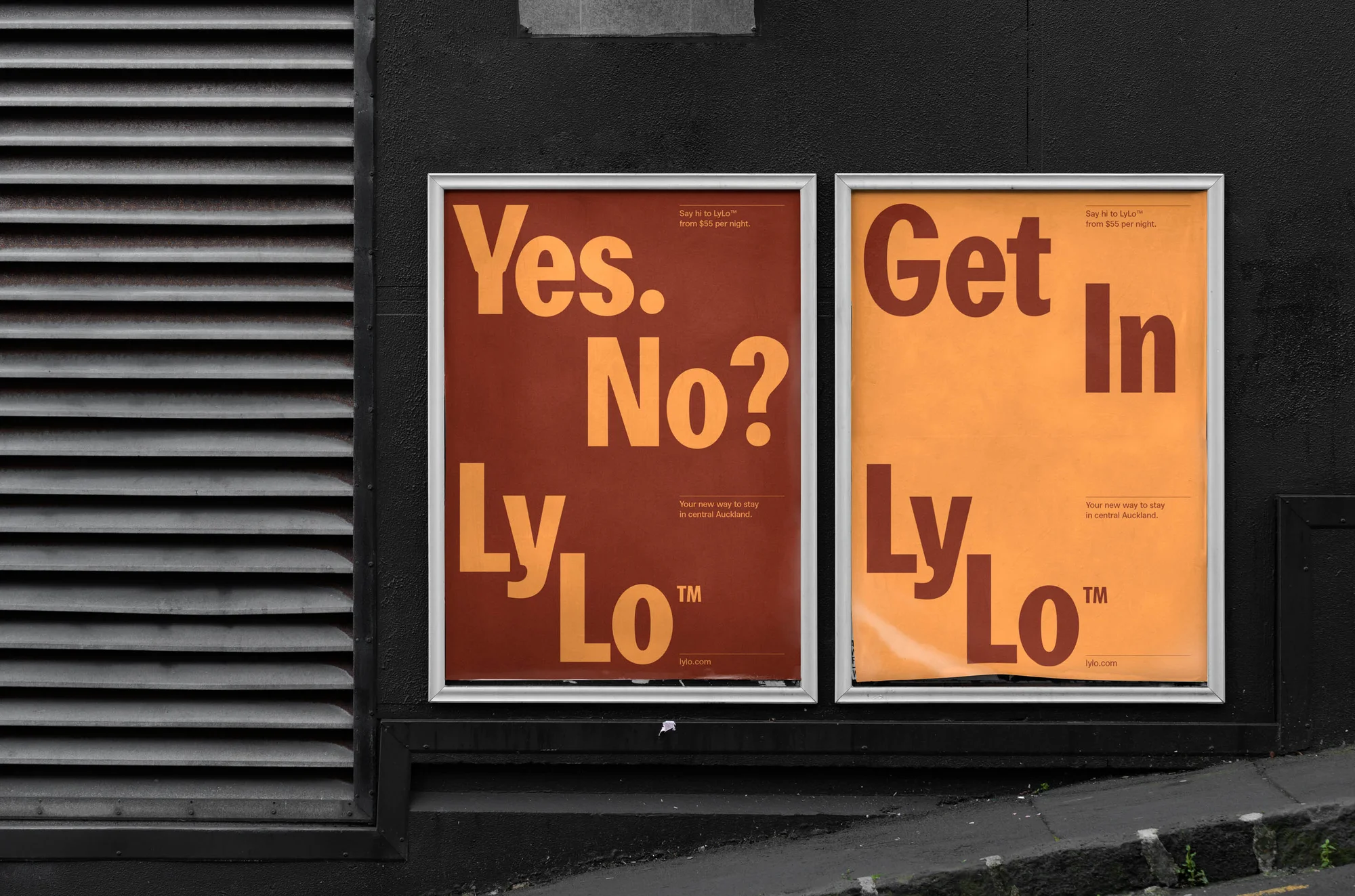 Two framed hotel advertisements featuring bold typography spelling "LyLo" in orange and brown tones are mounted on a gray wall.