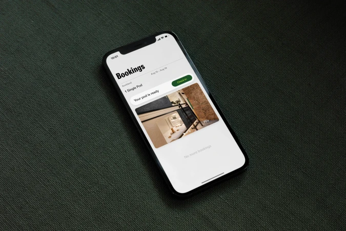 Close-up of a smartphone displaying a hotel booking app interface, with 'Bookings' heading and accommodation details on a textured surface.