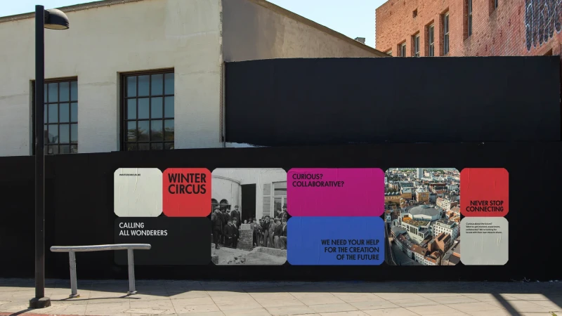 A modern public art installation on a city street displays colorful graphic posters with architectural and urban design themes on a black wall.