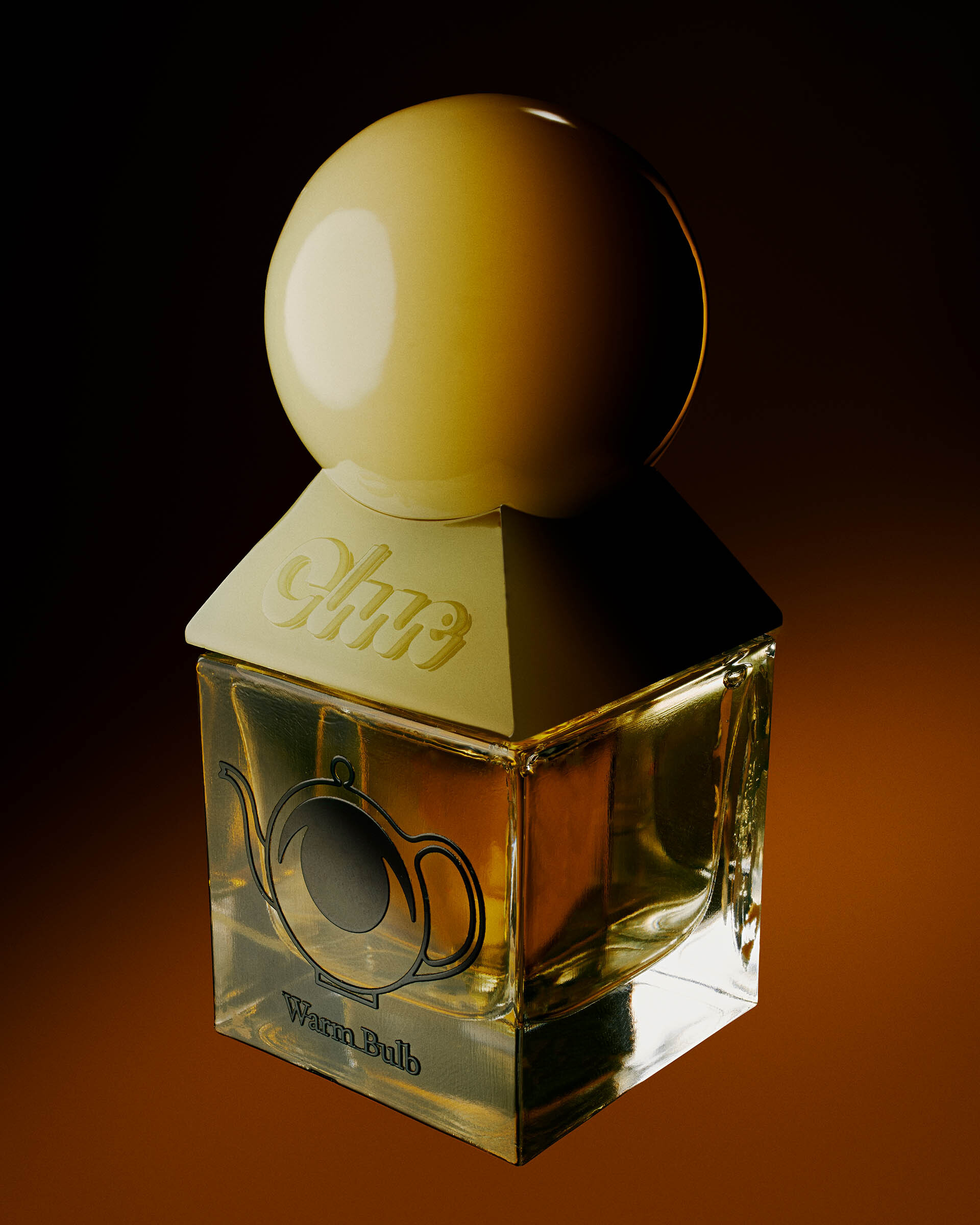 Close-up of a glass perfume bottle with a sphere top, adorned with a teapot graphic, set against a dark, warm-toned background.