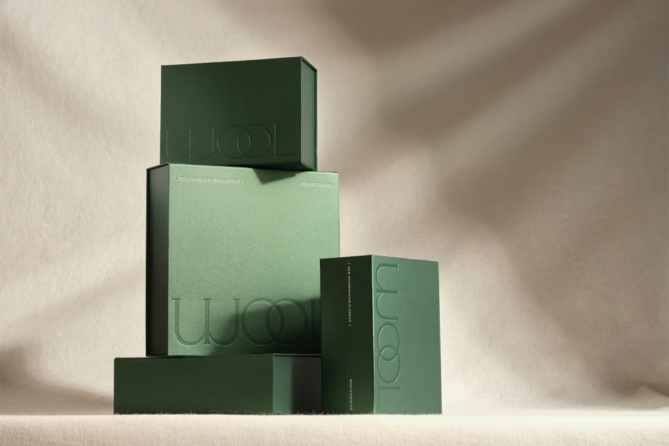 Stack of green boxes with embossed lettering in a studio setting, featuring product packaging design with a neutral background.