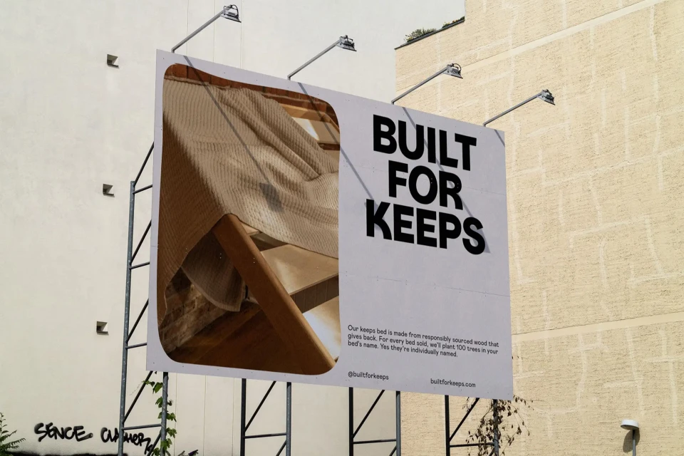 Billboard displaying bed frame ad with neutral-toned bedding in front of building, text reads: Built for Keeps.