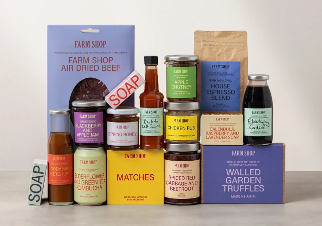 Assortment of Farm Shop food and bath products including dried beef, soap, jams, hot sauce, chutney, coffee, and truffles, packaged on a neutral surface.