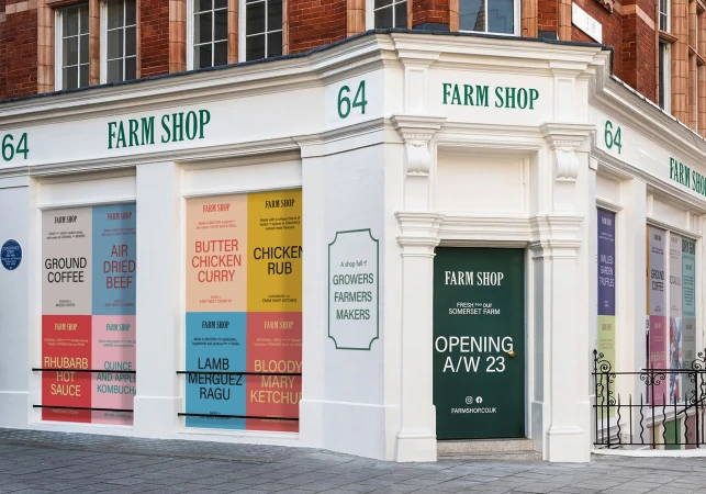 The exterior of a 'Farm Shop' storefront is captured on a sunny day, featuring large window displays with colorful food advertisements.