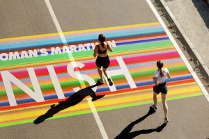 Two women running on an asphalt road over a colorful painted finish line graphic for Every Woman's Marathon.