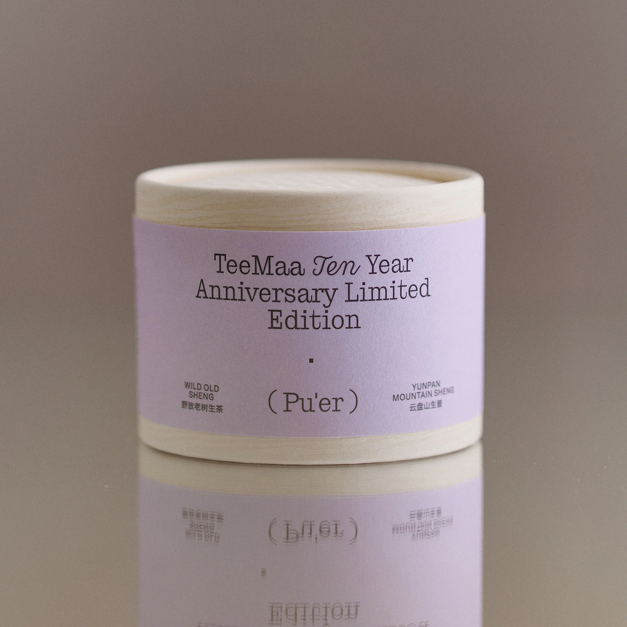 TeeMa Ten Year Anniversary Limited Edition Pu'er tea in a round container with a beige lid and lavender label on a reflective surface.