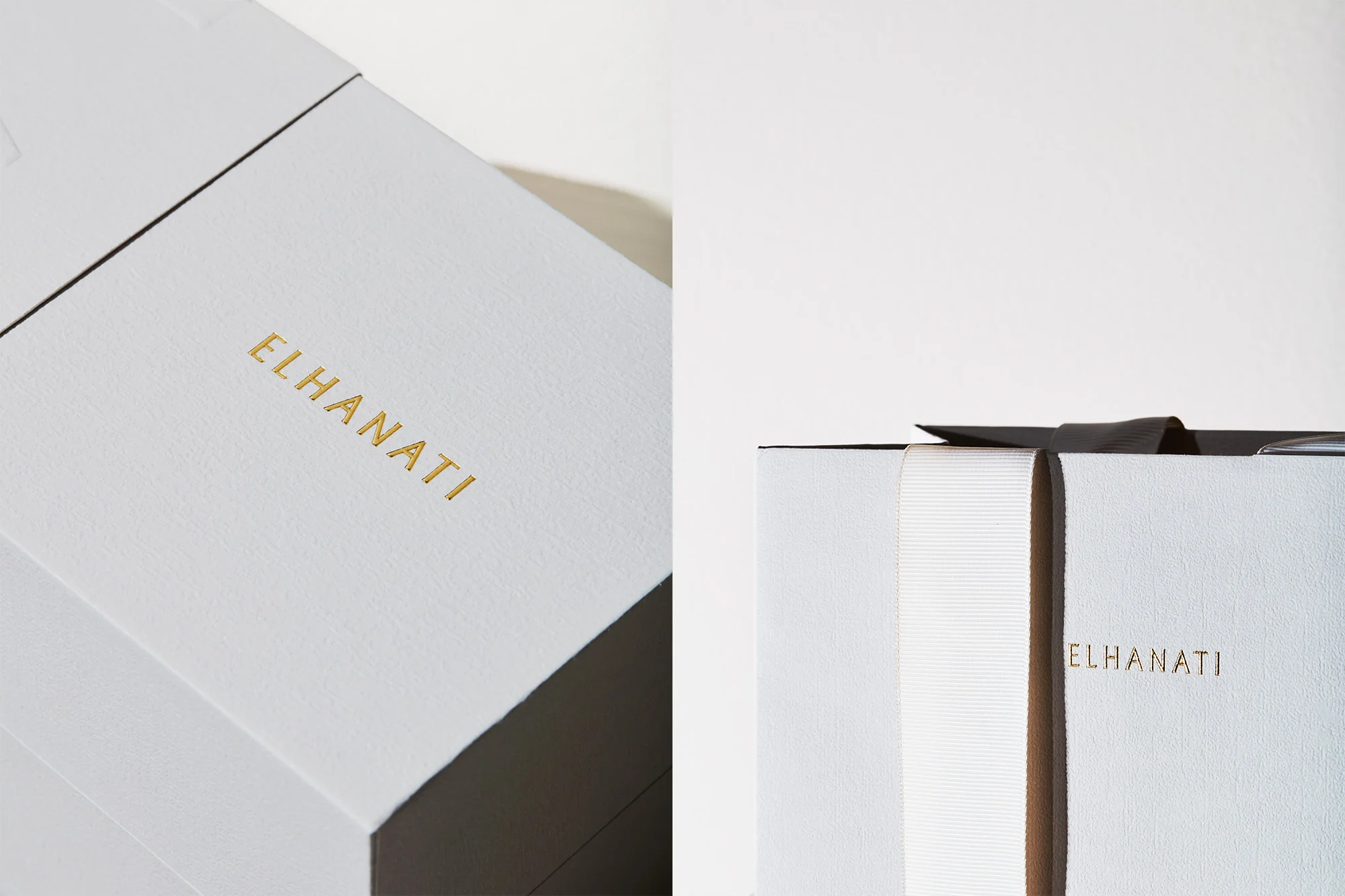Close-up of El Hanati branded gift boxes with white textured exteriors and golden lettering, accented by a white ribbon and a dark ribbon.
