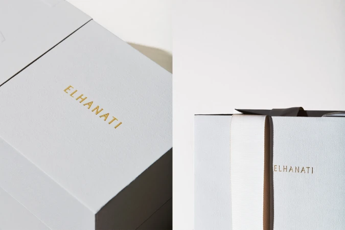 Close-up of luxury grey packaging boxes featuring embossed gold brand lettering and a white ribbon against a neutral background.