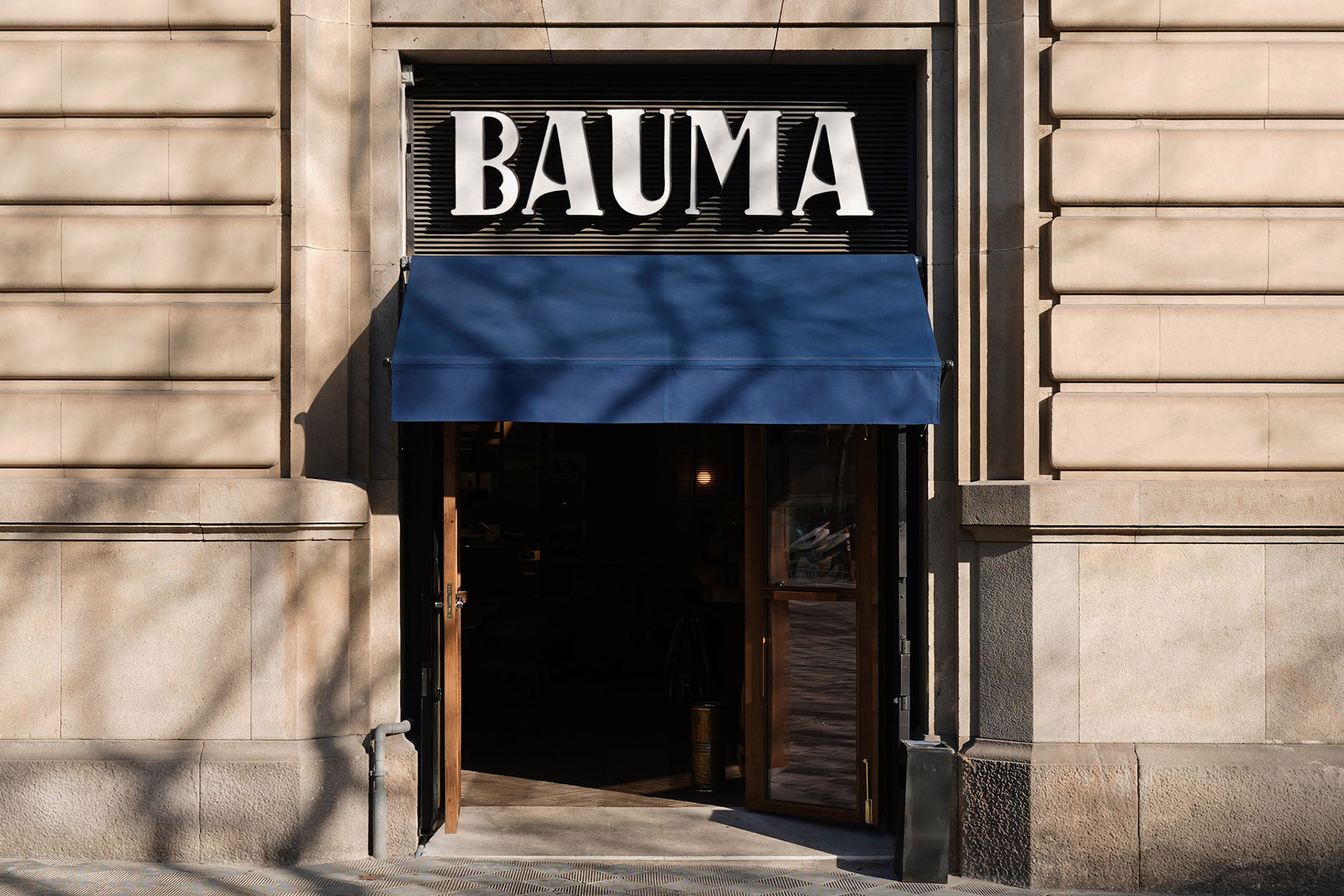 Facade of a stone building with a dark blue awning covering the entrance and the word 'BAUMA' in white letters above it.