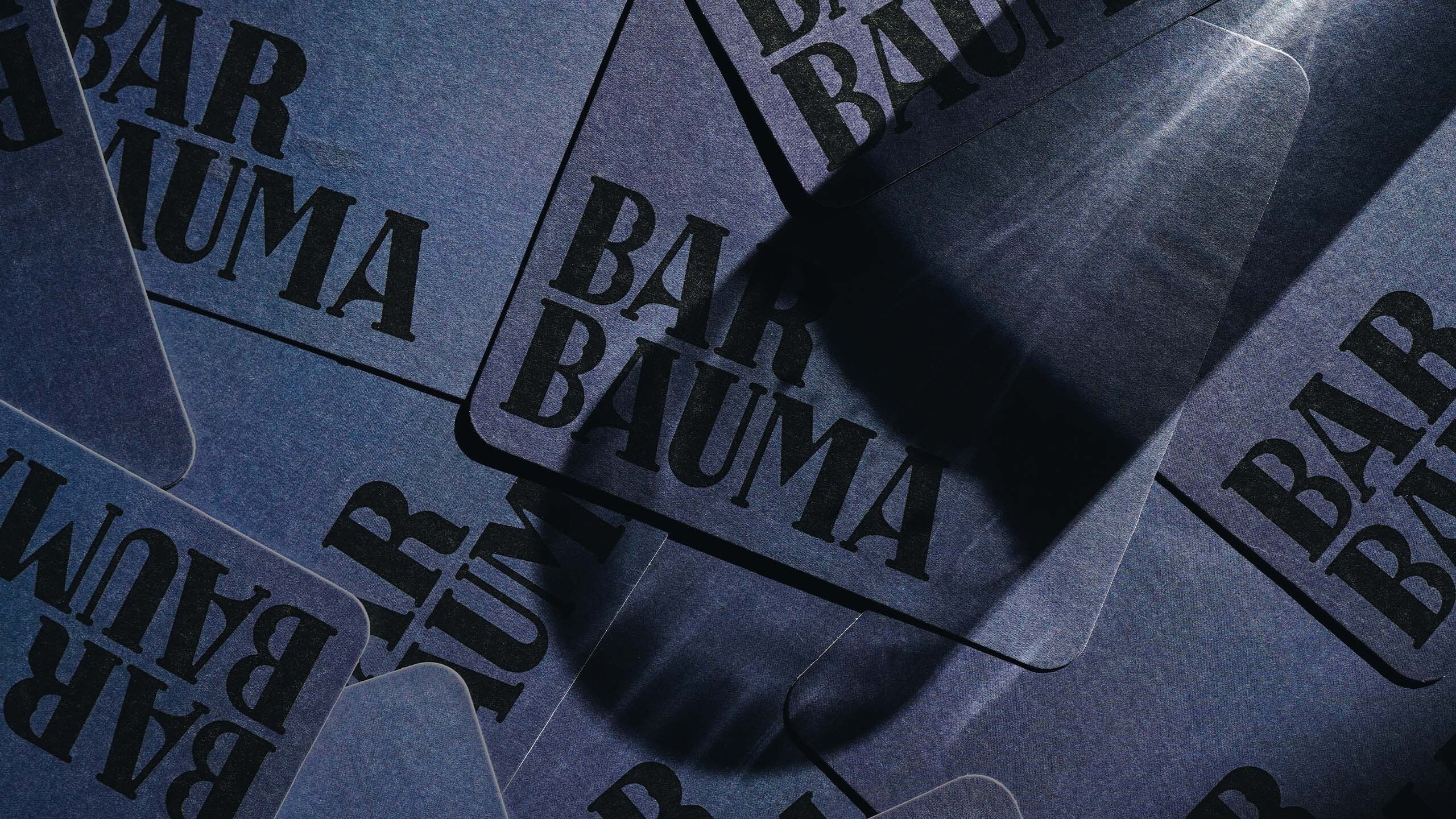 Promotional image displaying several blue-toned coasters with 'Bar Bauma' printed in bold black lettering.