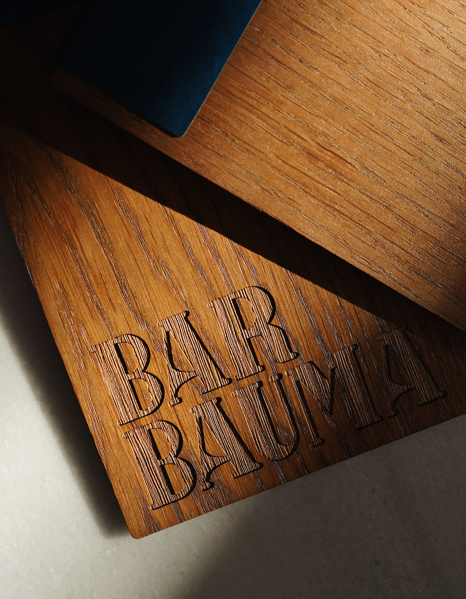 Close-up of a wooden surface engraved with 'BAR BAUMA,' showcasing detailed wood grain and modern design under soft, directional lighting.
