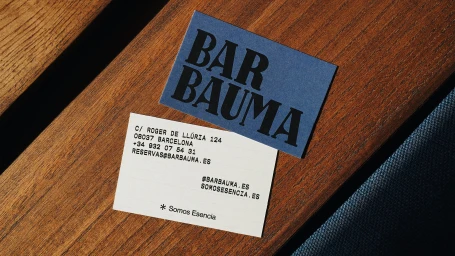 Two business cards for Bar Bauma resting on a warm wooden tabletop with blue upholstery visible.