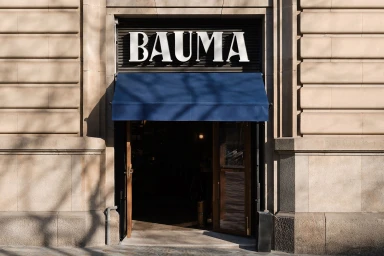 Exterior storefront of Bar Bauma featuring bold white BAUMA lettering above a blue awning and open wooden doors.