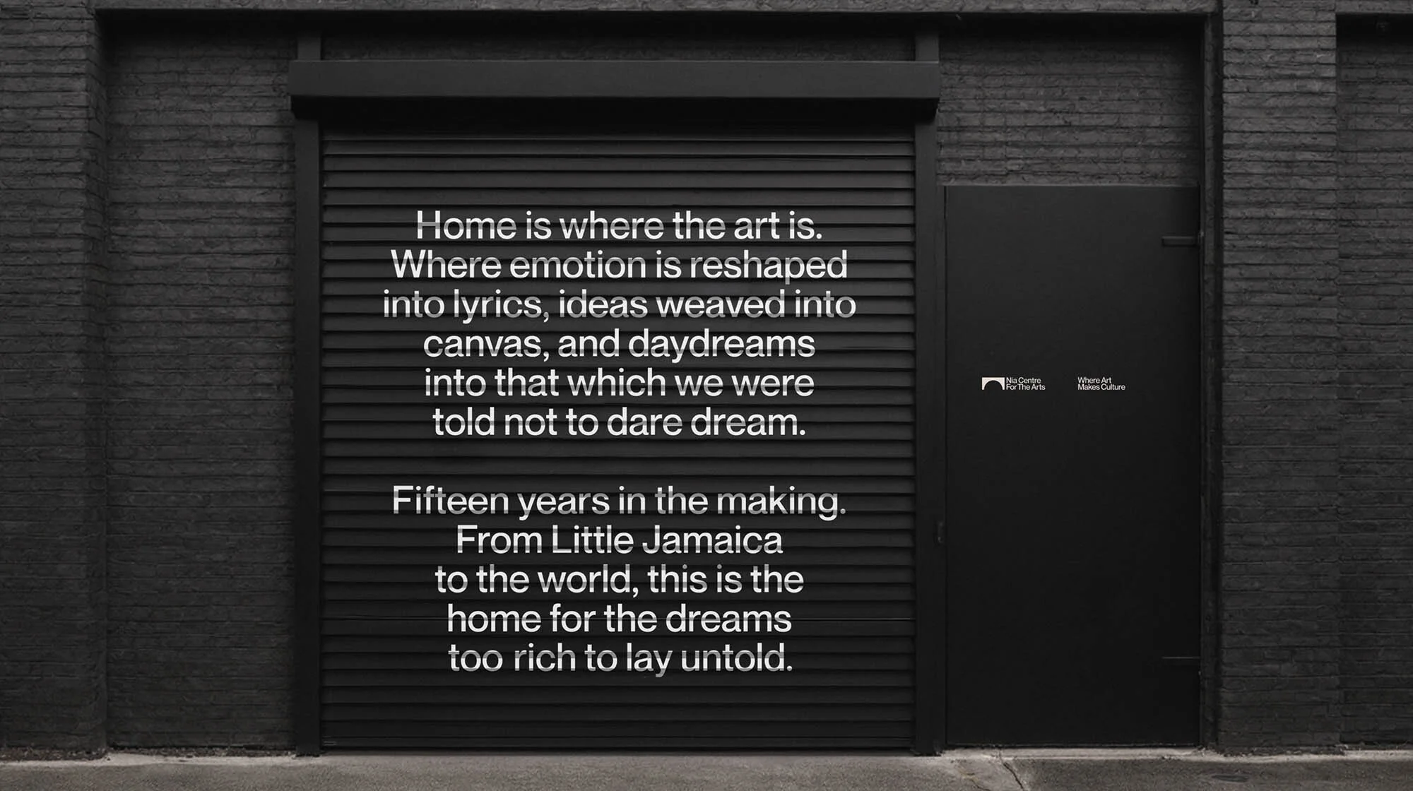 Black brick wall with a roll-up garage door and a standard door, both painted black, with a white text overlay featuring art quotes.