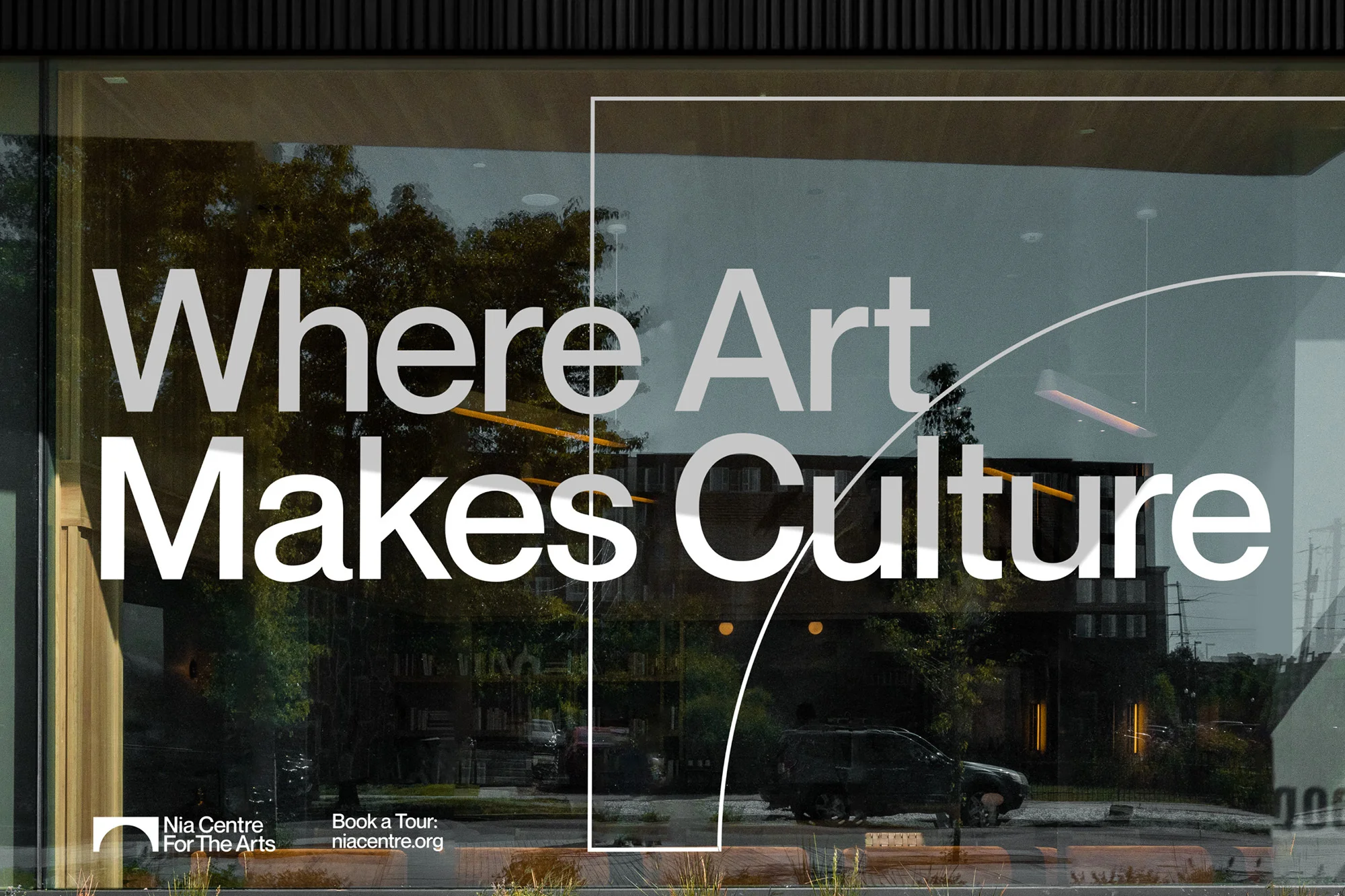 Building facade with window decal: 'Where Art Makes Culture,' Nia Centre For The Arts logo, reflecting the surrounding greenery and street.