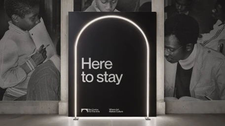 Black promotional sign with an illuminated arch outline and white typography reading Here to stay for Nia Centre brand identity