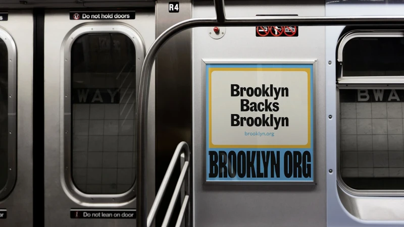 Interior view of a subway car with brushed metal doors and an advertisement for Brooklyn, featuring bold text and a website address.