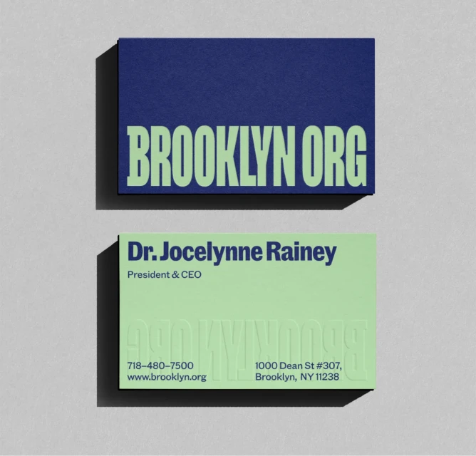 Two business cards, one navy with 'BROOKLYN ORG' in green, the other mint green with contact details, laid on a grey surface.
