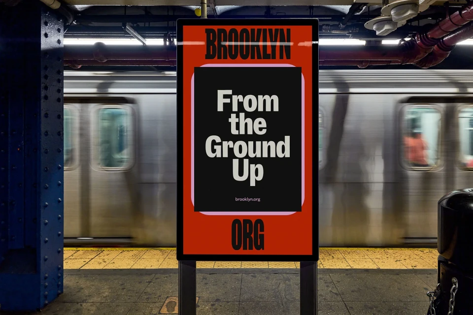 Brooklyn subway station ad featuring the words 'From the Ground Up' in bold white letters with a blurred train passing in the background.
