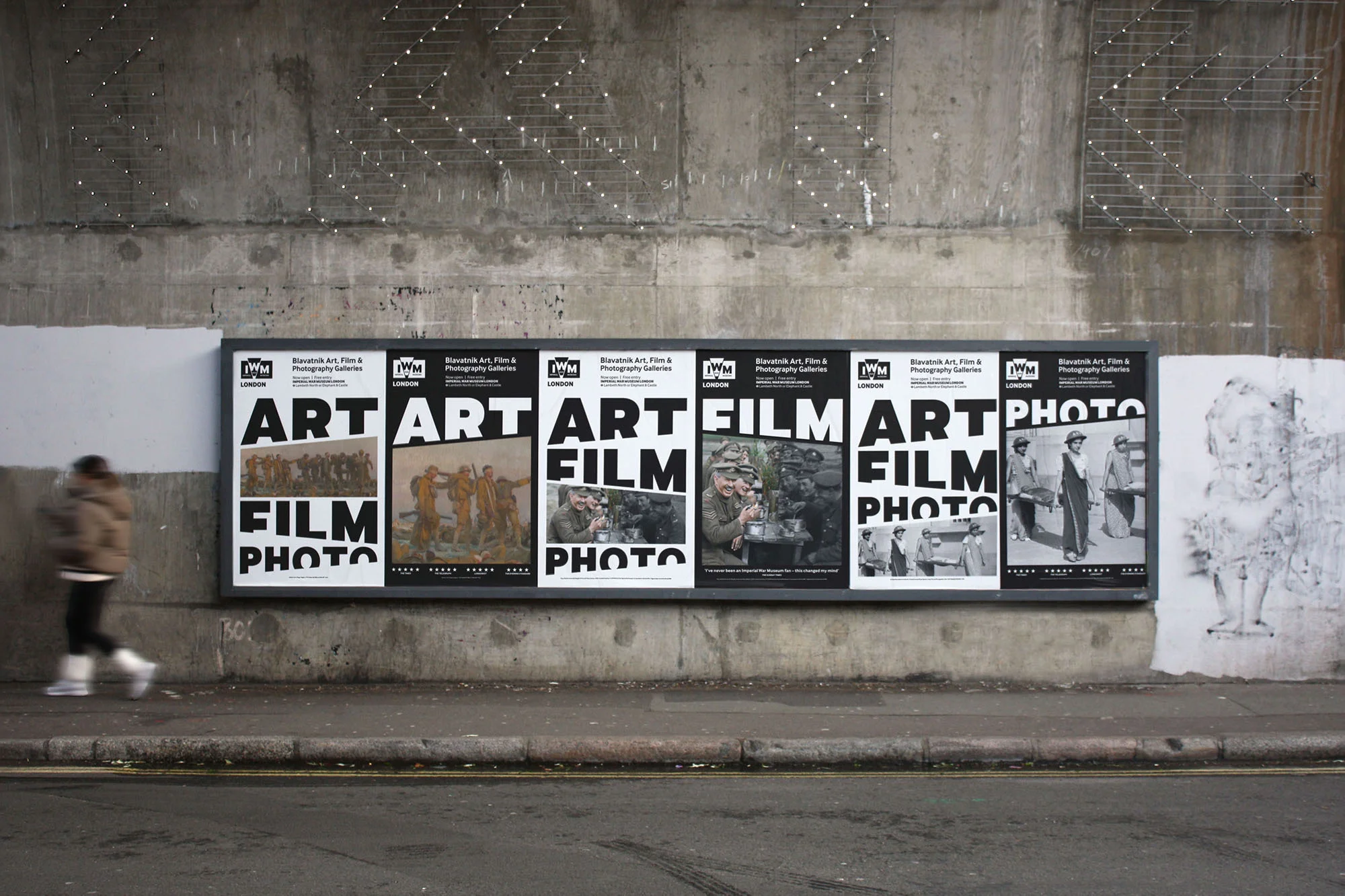 Public art installation featuring a series of black and white posters with text reading 'Art Film Photo' displayed on a concrete wall.