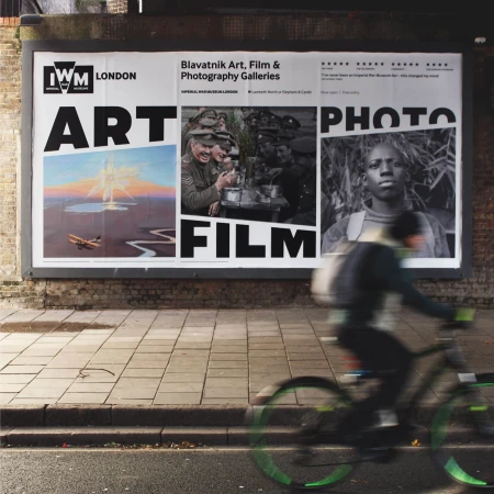 Street-level view of a large billboard advertising Blavatnik Art, Film & Photography Galleries, with a blurred bicyclist passing by.