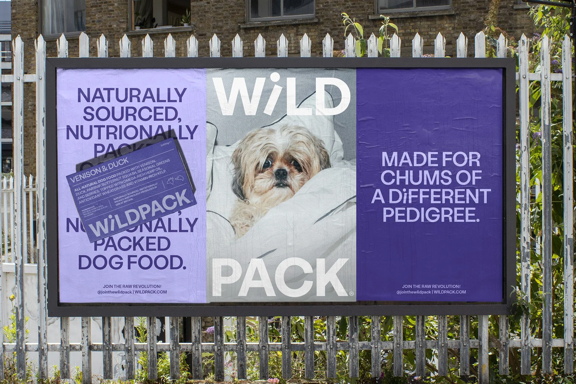 Dog food advertising billboard shows a cute dog wrapped in a white blanket, with product information and branding; white picket fence background.