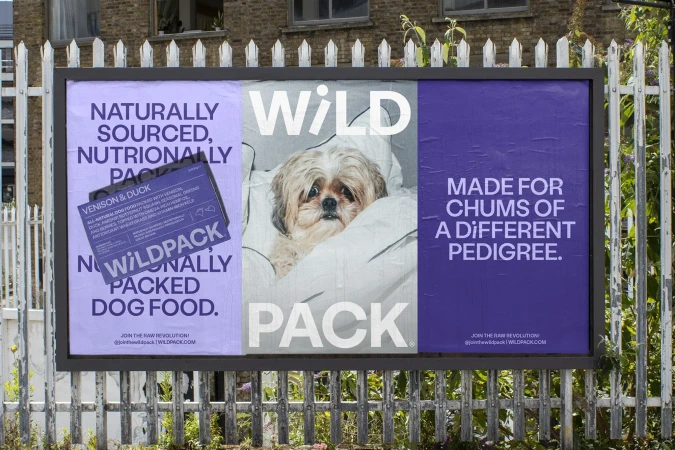Dog food advertising billboard shows a cute dog wrapped in a white blanket, with product information and branding; white picket fence background.