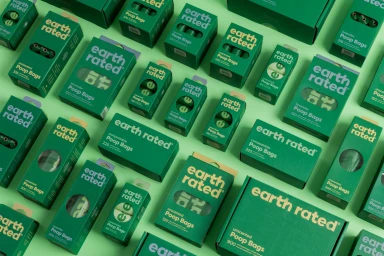 Top-down flat lay of green Earth Rated poop bag boxes and packaging arranged in a grid pattern against a light green background.