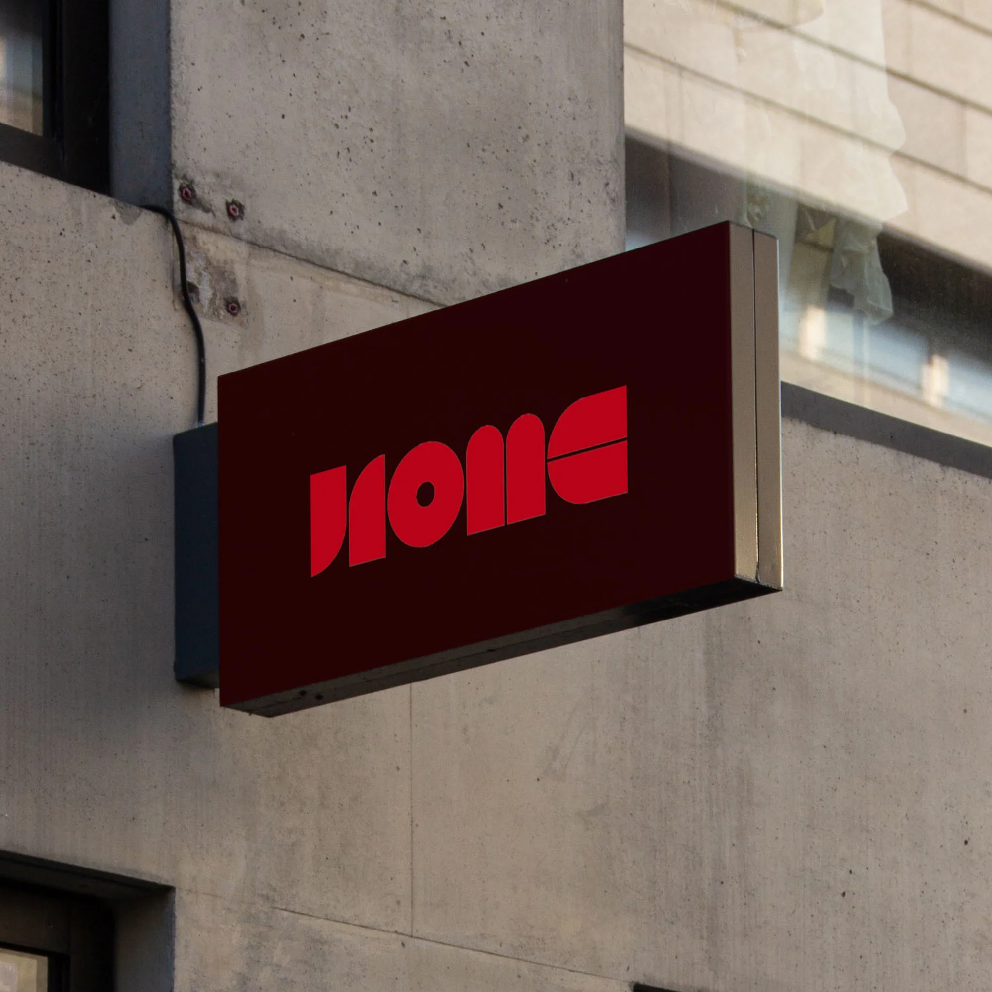 Exterior view of a building with a dark red business sign featuring large, stylized red lettering on a rectangular box.