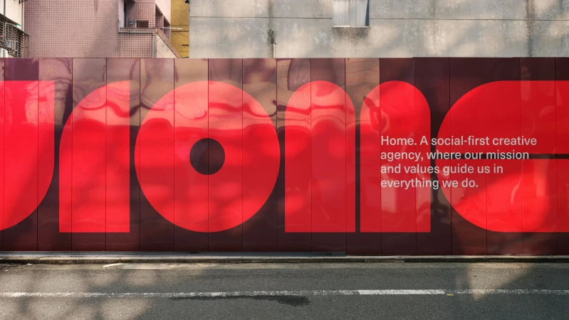 Exterior shot of a building wall with a large red text logo and mission statement against a brown background in an urban setting.
