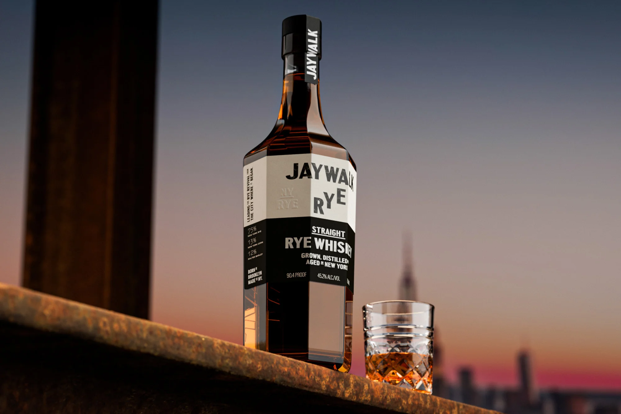 JayWalk rye whiskey bottle with straight rye whiskey in a glass with a city skyline in the background at dusk.