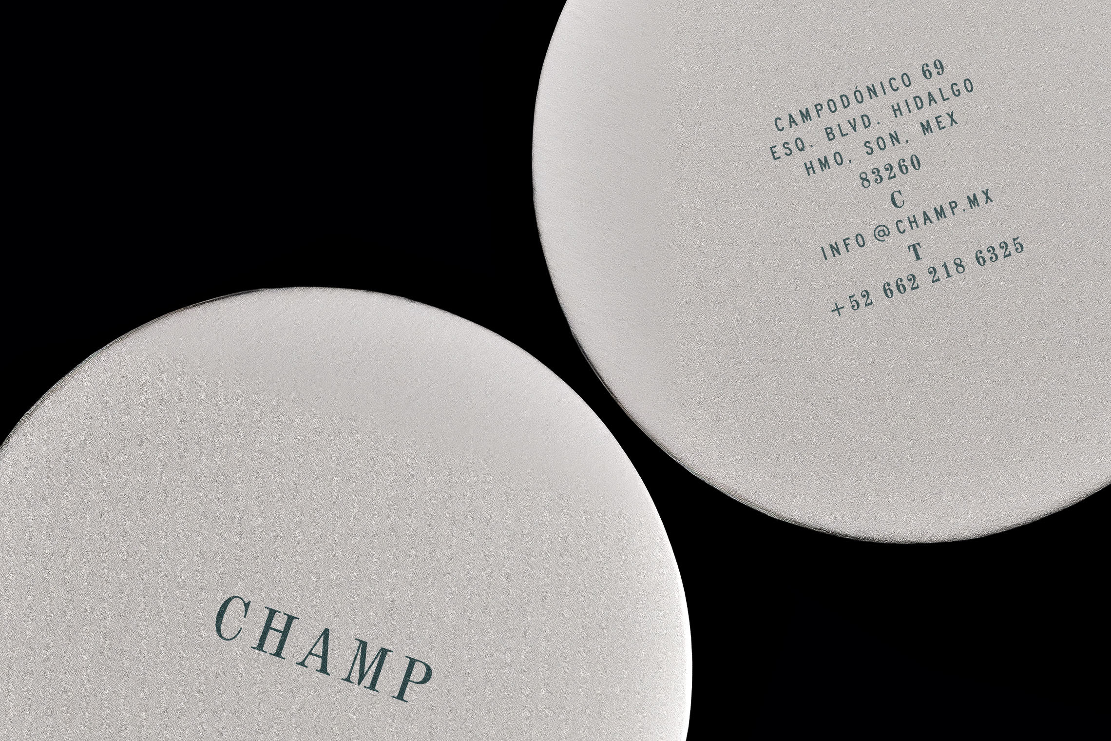 Close-up studio shot of two round, textured coasters, one featuring 'CHAMP' in dark green text against a black background.