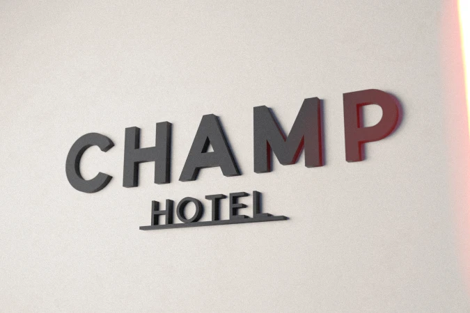 A gray 'Champ Hotel' sign is mounted on a white wall, slightly angled and lit by ambient light with an orange color cast on the right edge.