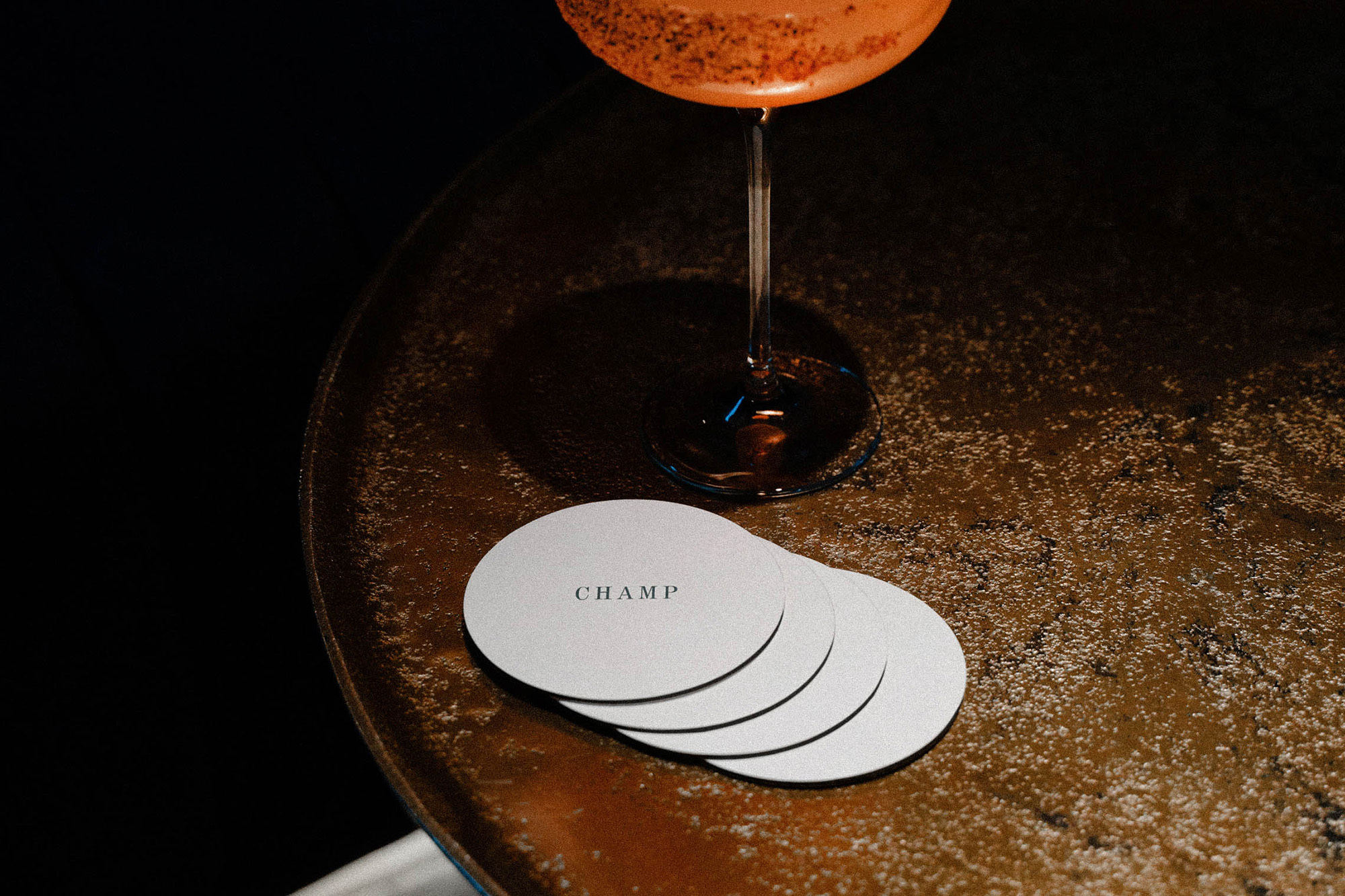 Cocktail with glass and coasters on a brown textured table with dark background, showcasing a dimly lit, upscale ambiance.