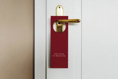 Red door hanger reading Por Favor No Molestar hanging on a brass handle of a white door