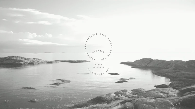 Monochrome landscape shot of rocky shoreline, calm water, and cloudy sky. A circular text overlay with brand name and tagline.