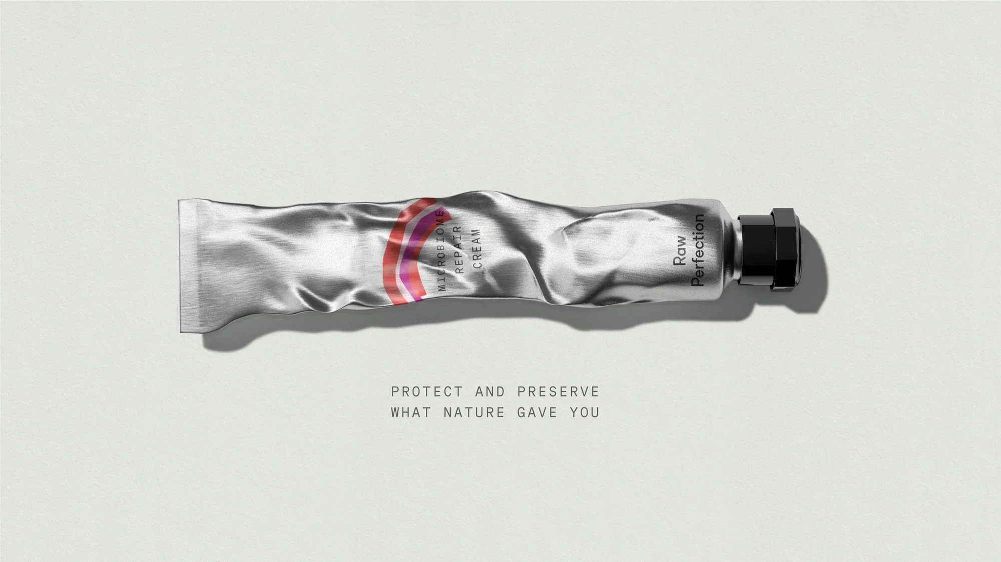 Cosmetic cream tube in horizontal orientation on a light gray surface. 'Raw Perfection' skincare product for microbiome repair.