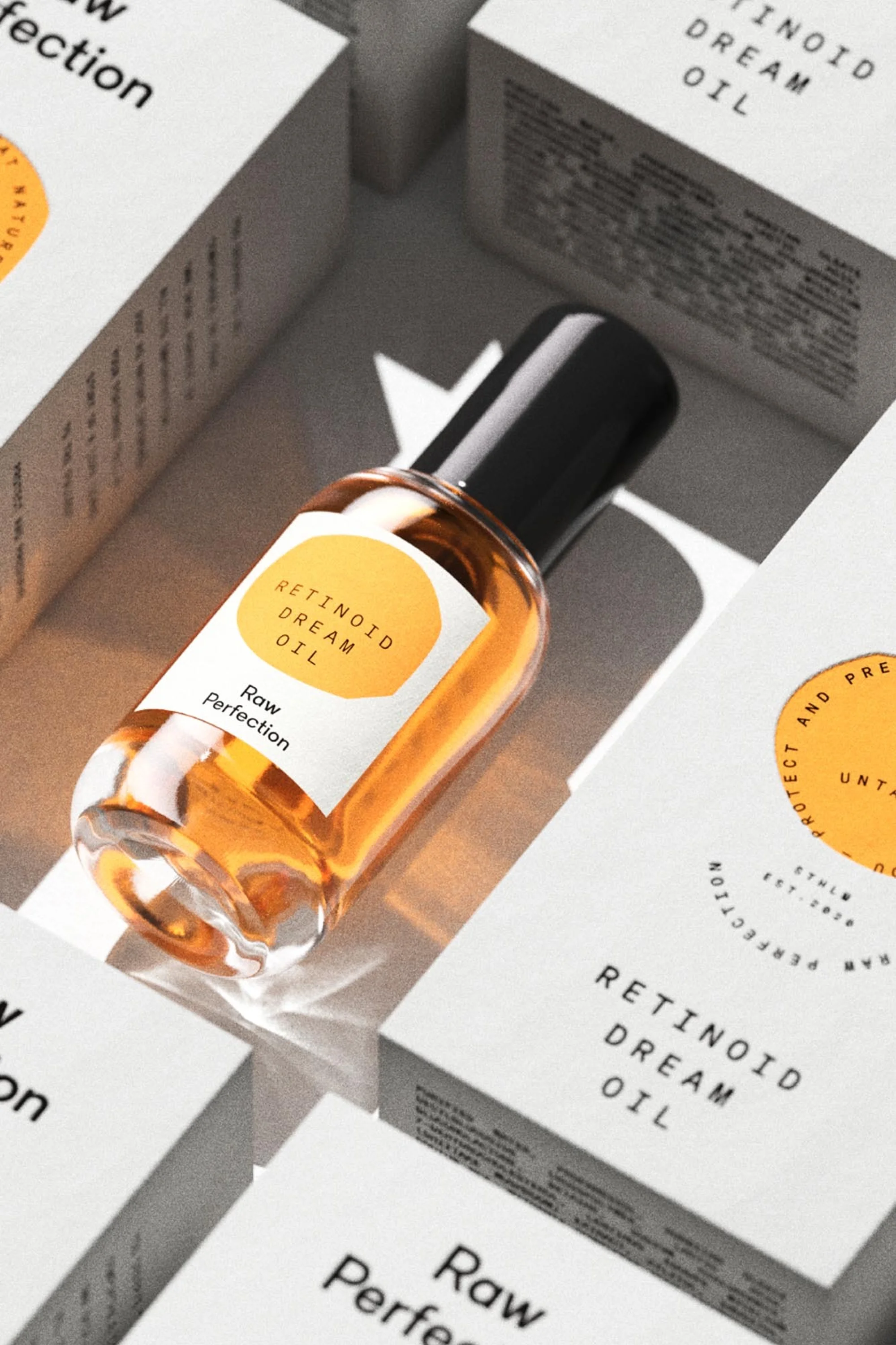 Close-up of a bottle of Retinoid Dream Oil surrounded by boxes with similar branding and text, on a light surface and background.