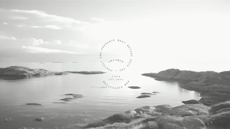 Monochrome landscape showing rocky coastlines along a calm sea under a bright overcast sky, centered circular brand typography