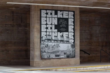Large black and white typography poster mounted on a concrete pillar beneath a brutalist architectural structure