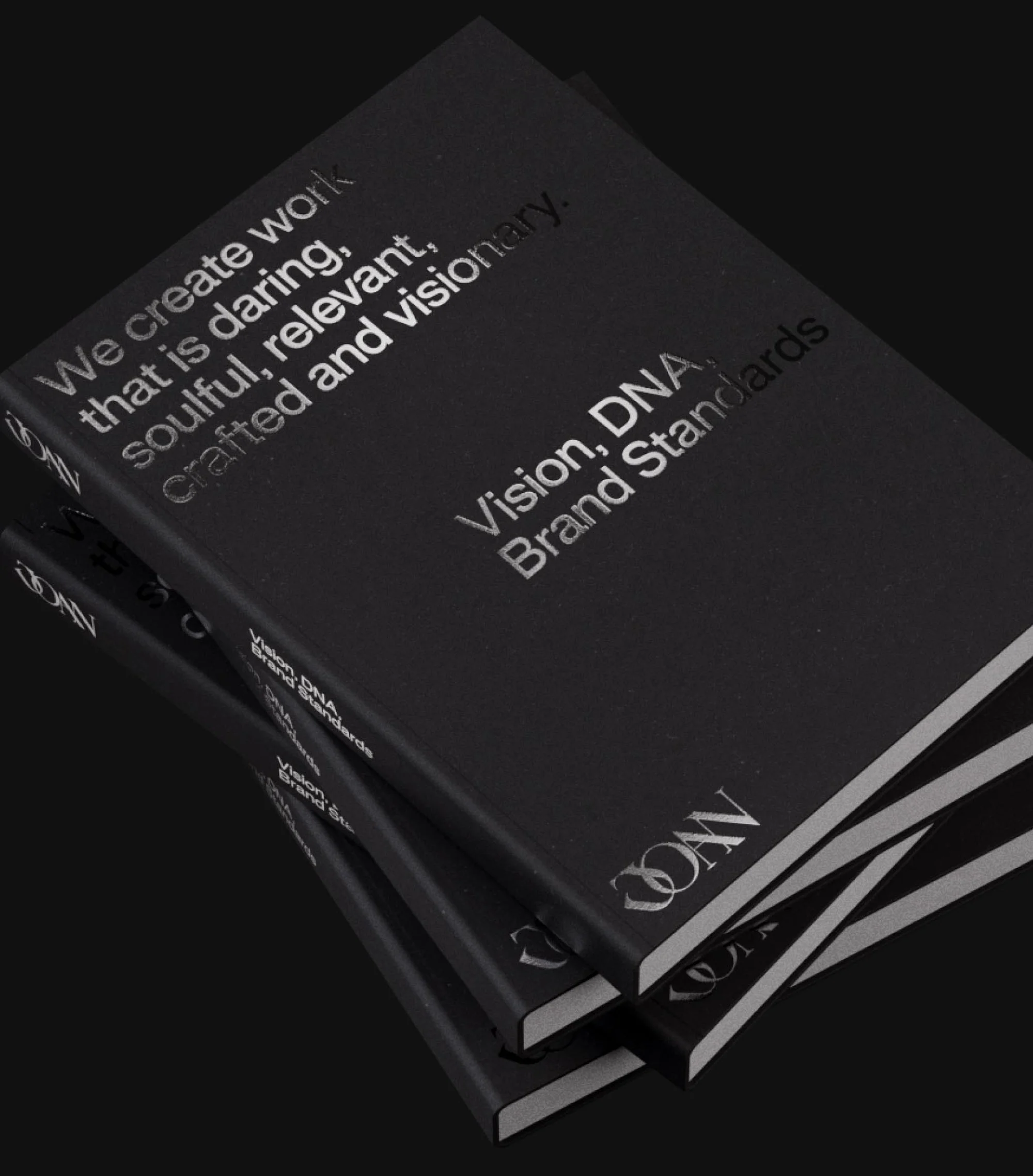 Three black books stacked displaying silver text reading 'Vision, DNA, Brand Standards' on a black background.