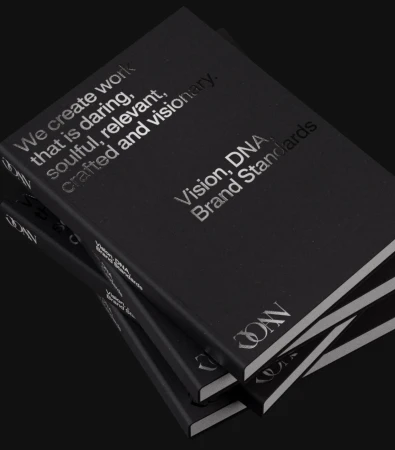 Three black books stacked displaying silver text reading 'Vision, DNA, Brand Standards' on a black background.