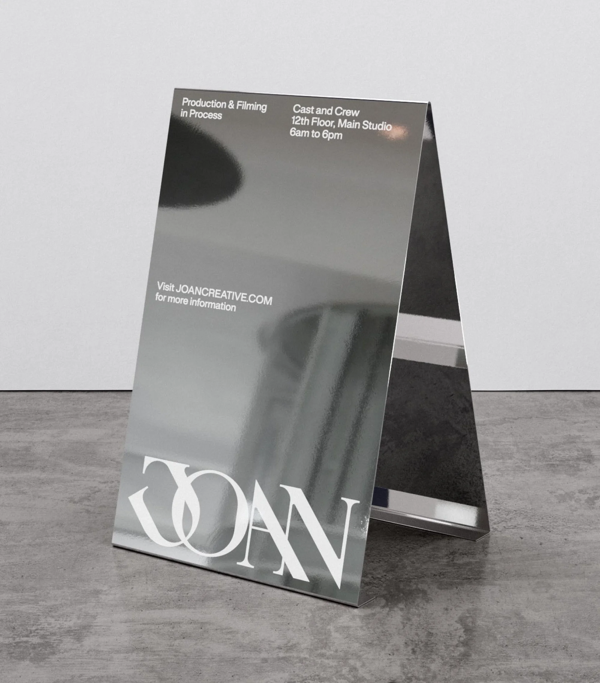 A silver, A-frame sign sits indoors on a gray concrete floor, advertising film production information with visible text and reflections.