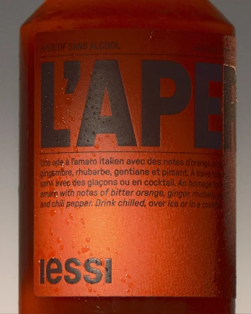 Close-up of a vibrant orange bottle featuring 'L'Apéritif' label, adorned with condensation droplets, showcasing an enticing non-alcoholic beverage.
