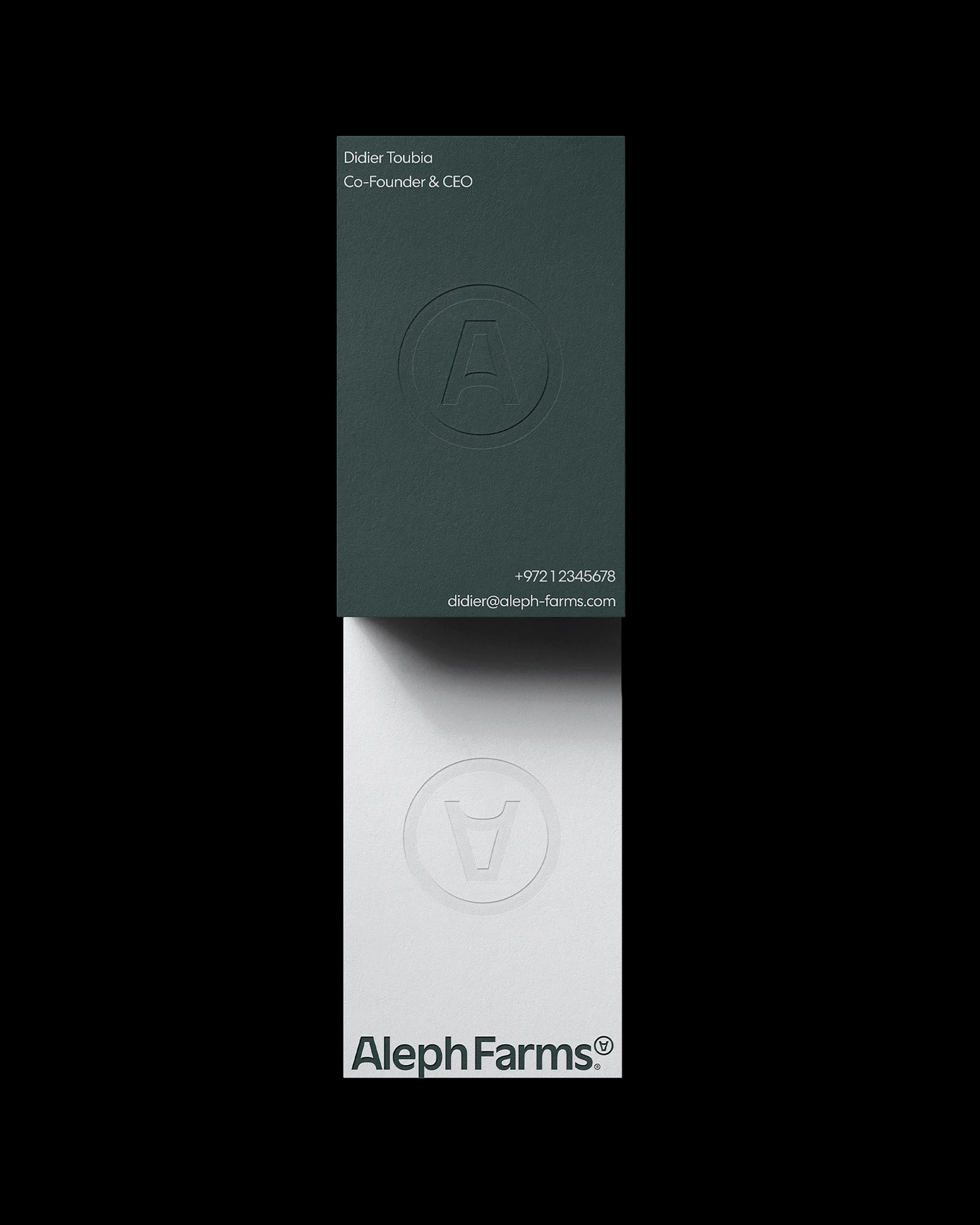Elevated studio shot of two business cards in a vertical stack, one green with embossed logo and one white with printed logo.